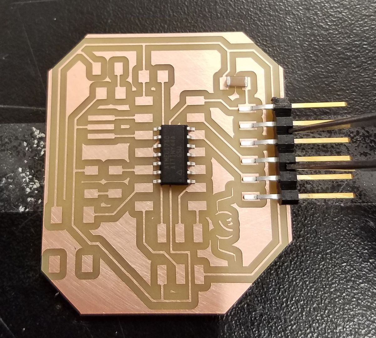 photo of milled copper circuit board with microprocessor seated on pads much too large for it, while a 6 pin header and capacitor fit comfortably in their pads